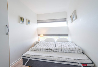 Dormitorio luminoso y compacto con cama doble, decoración moderna y ventana en una casa flotante en Hemmet, Dinamarca.