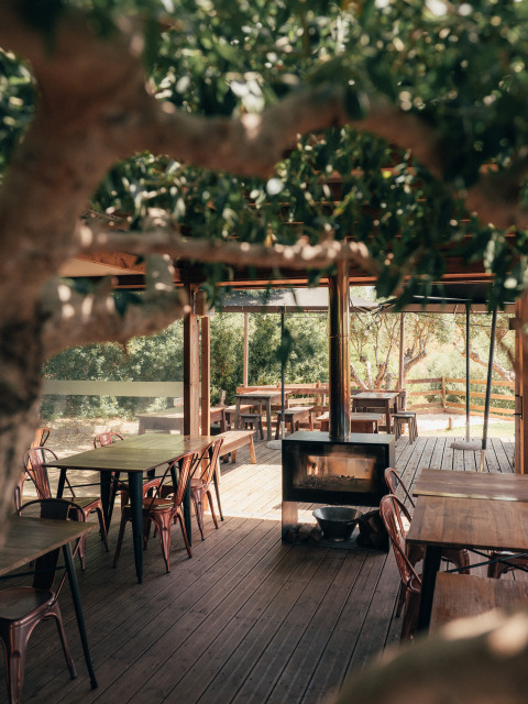 Udendørs spiseområde med træmøbler og pejs, omgivet af grønne træer på Wecamp Reserva Alecrim i Alentejo.