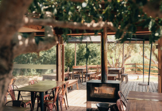 Gezellig buitenterras met houten tafels en haardvuur bij Wecamp Reserva Alecrim, Alentejo, Portugal.