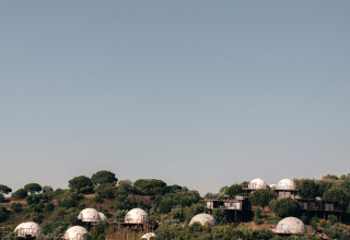 Wecamp Reserva Alecrim in Alentejo, Portugal, met koepeltenten op een groene heuvel en blauwe lucht erboven.