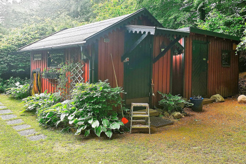 Rood houten vakantiehuis voor 4 personen in Tjörnarp, omgeven door planten en groene tuin.