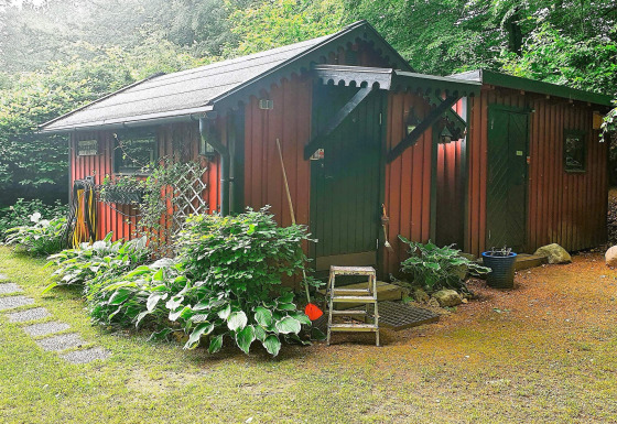 Rote Holzhütte im Grünen bei Tjörnarp, umgeben von Pflanzen und Bäumen, für 4 Personen geeignet.