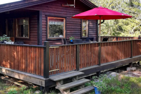 Buitenaanzicht van een houten vakantiehuis met terras, rood hek en parasol in Norrtälje, Zweden.
