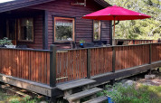 Buitenaanzicht van een houten vakantiehuis met terras, rood hek en parasol in Norrtälje, Zweden.