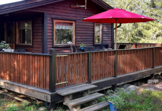 Vue extérieure d'une maison de vacances en bois avec terrasse, rambarde et parasol rouge à Norrtälje, Suède.