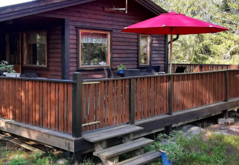 Buitenaanzicht van een houten vakantiehuis met terras, rood hek en parasol in Norrtälje, Zweden.