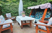 Buitenzitje bij een vakantiehuis in TJÖRNARP, Zweden, met tuinschommel en stoelen met blauwe kussens.