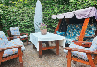 Buitenzitje bij een vakantiehuis in TJÖRNARP, Zweden, met tuinschommel en stoelen met blauwe kussens.