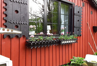 Cornice nera e persiane artistiche su casetta rossa con piante fiorite a Tjörnarp, Svezia.