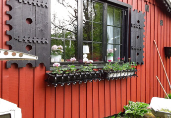 Cadre de fenêtre noir, volets décoratifs et jardinière sur un chalet rouge à Tjörnarp, Suède.