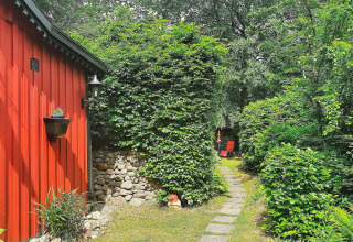 Garten mit Steinweg und roten Stühlen bei einer roten Hütte in Tjörnarp, Schweden, umgeben von Grün.