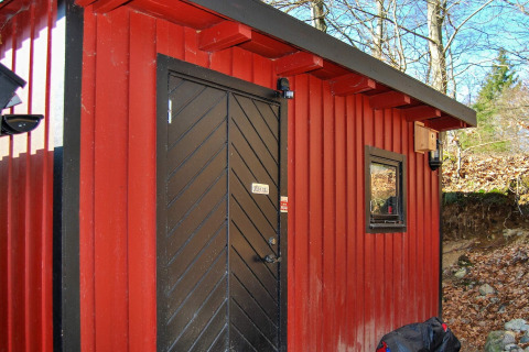Rood huisje met zwarte deur en raam in Tjörnarp, Zweden, omgeven door herfstbomen en bladeren.