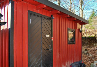 Casetta rossa con porta e finestra nere a Tjörnarp, Svezia, circondata da alberi e foglie autunnali.