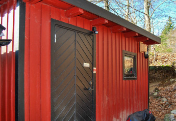 Rote Hütte mit schwarzer Tür und Fenster in Tjörnarp, Schweden, umgeben von Wald im Herbst.