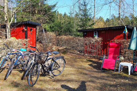 Rode huisjes met fietsen, ligstoel en parasol bij een vakantiehuis in Tjörnarp, Zweden, omringd door bos.