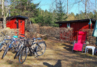 Rode huisjes, fietsen, een ligzetel en parasol bij een vakantiehuis in Tjörnarp, Zweden, omringd door bos.
