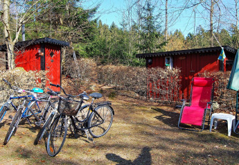 Rote Hütten mit Fahrrädern, Liegestuhl und Sonnenschirm vor Ferienhaus in Tjörnarp, Schweden.