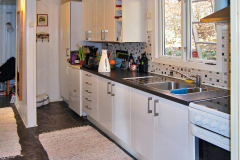 Cucina moderna di casa vacanza a Tjörnarp, Svezia, con mobili bianchi, piano nero e grande finestra.