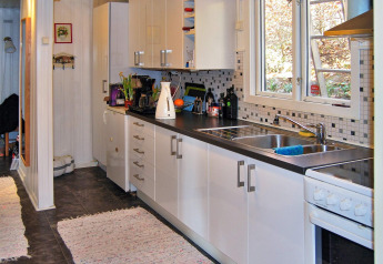 Moderne vakantiehuiskeuken in Tjörnarp, Zweden, met witte kasten, zwart aanrecht en grote ramen.