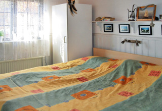 Slaapkamer met bont beddengoed, raam met gordijnen, witte kast en een plank met foto's in een hut.