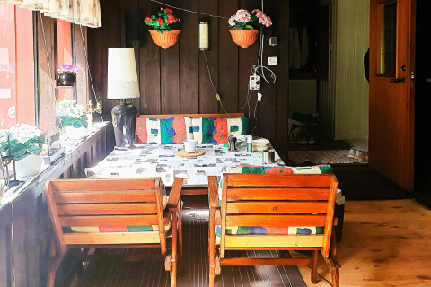 Accogliente zona pranzo in baita con sedie di legno, cuscini colorati e fiori in vaso alla finestra.