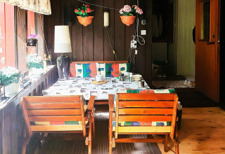Accogliente zona pranzo in baita con sedie di legno, cuscini colorati e fiori in vaso alla finestra.
