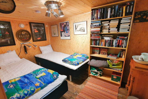 Knusse houten blokhutkamer in Zweden met twee eenpersoonsbedden, boekenrek en kleurrijke dekens.