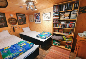 Gezellige houten cabin in Zweden met twee eenpersoonsbedden, boekenkast, kleurrijk beddengoed en kunst.