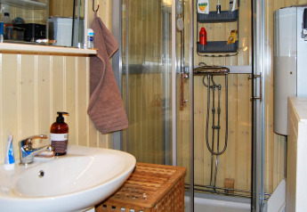 Wood-paneled bathroom with shower, sink, towel and toiletries in a cabin in Tjörnarp, Sweden.