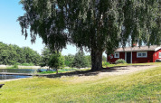 Ferienhaus in Norrtälje, Schweden, mit rotem Haus, See, Badesteg und grünem Ufer bei Sonne.