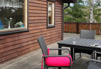 Houten terras met zwart tuinmeubilair, felroze kussen en uitzicht op bos bij vakantiehuis in Norrtälje.