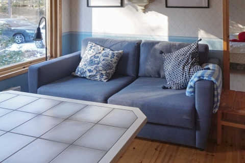 Wohnzimmer mit blauer Couch, gemusterten Kissen und weißem Tisch in einem Ferienhaus in Norrtälje, Schweden.