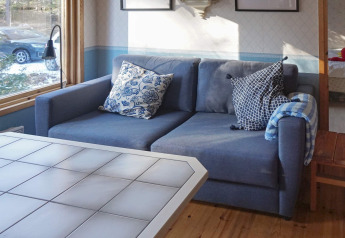 Wohnzimmer mit blauer Couch, gemusterten Kissen und weißem Tisch in einem Ferienhaus in Norrtälje, Schweden.