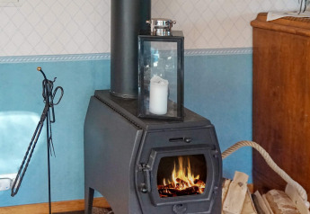 Houtkachel met lantaarn en kaars erop, haardhout en gereedschap ernaast, in een lodge in Norrtälje, Zweden.