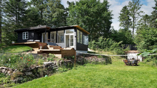 El alojamiento vacacional para 6 personas en Melby, una cabaña negra rodeada de jardín y bosque.