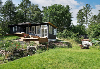 El alojamiento vacacional para 6 personas en Melby, una cabaña negra rodeada de jardín y bosque.