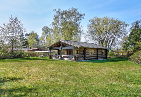 Houten lodge voor 6 personen in Eskebjerg, omgeven door gras, bomen en een charmant overdekt terras.