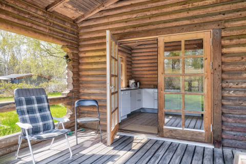 Blokhut met open deuren naar kleine keuken, twee stoelen op de veranda en groen in Eskebjerg, Denemarken