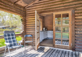 Blokhut met open deuren naar kleine keuken, twee stoelen op de veranda en groen in Eskebjerg, Denemarken
