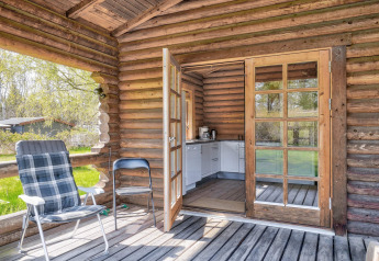 Houten lodge met open deur naar kleine keuken, twee stoelen op terras en groen in Eskebjerg, Denemarken