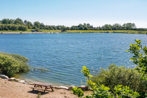 Zicht op een rustige vijver met picknickbank en groen bij de 6-persoonshuis in Eskebjerg, Denemarken.
