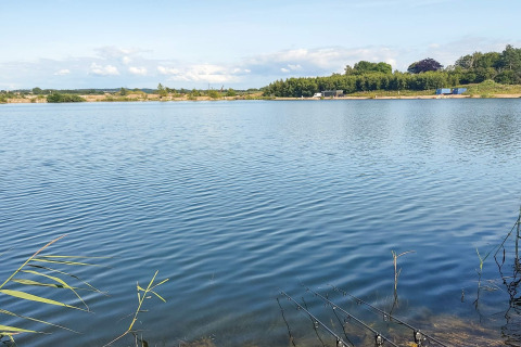 Vista di un lago calmo presso il 6-Person Home a Eskebjerg, Danimarca, con canne da pesca in primo piano.