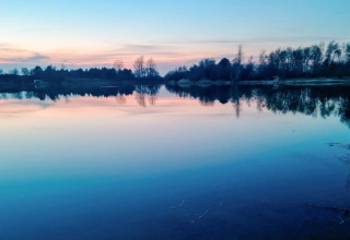 Lago tranquilo al atardecer cerca de una casa para 6 personas en Eskebjerg, Dinamarca, con reflejos de árboles.