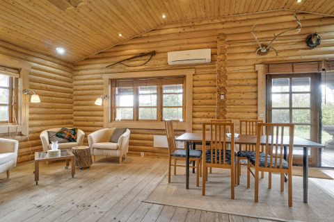 Lyst og hyggeligt opholdsrum i en bjælkehytte i Eskebjerg, Danmark, med spisebord og loungestole.