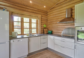 Heldere keuken in houten lodge met witte kasten, moderne toestellen en zicht op de tuin.