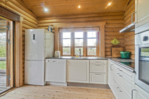 Helles Blockhaus-Küche mit weißen Schränken, Kühlschrank und Spülmaschine in Eskebjerg, Dänemark.