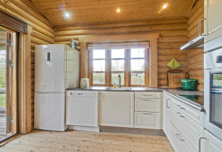 Helles Blockhaus-Küche mit weißen Schränken, Kühlschrank und Spülmaschine in Eskebjerg, Dänemark.
