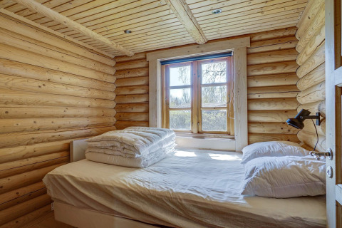 Schlafzimmer einer Blockhütte mit Doppelbett am Fenster, viel Holz, in Eskebjerg, Dänemark.