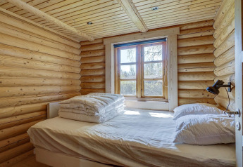 Slaapkamer in blokhut met tweepersoonsbed naast raam, zonlicht, in Eskebjerg, Denemarken.