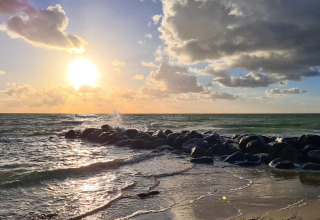 Smukt solnedgangsbillede over havet med skyer og sten ved stranden ved et feriehus i Melby, Danmark.